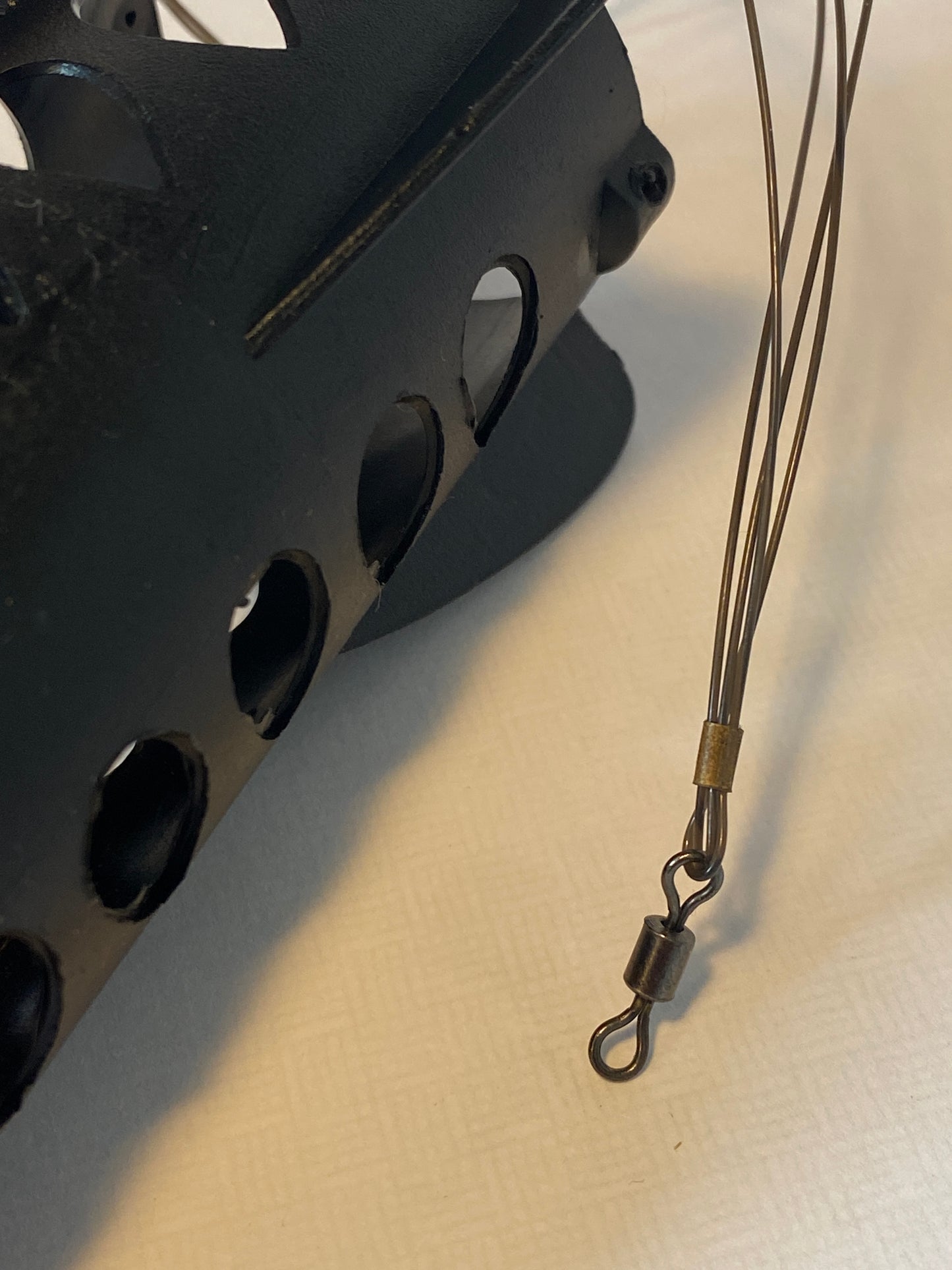 Fishing line with a swivel attached to a black spod rocket on a light background