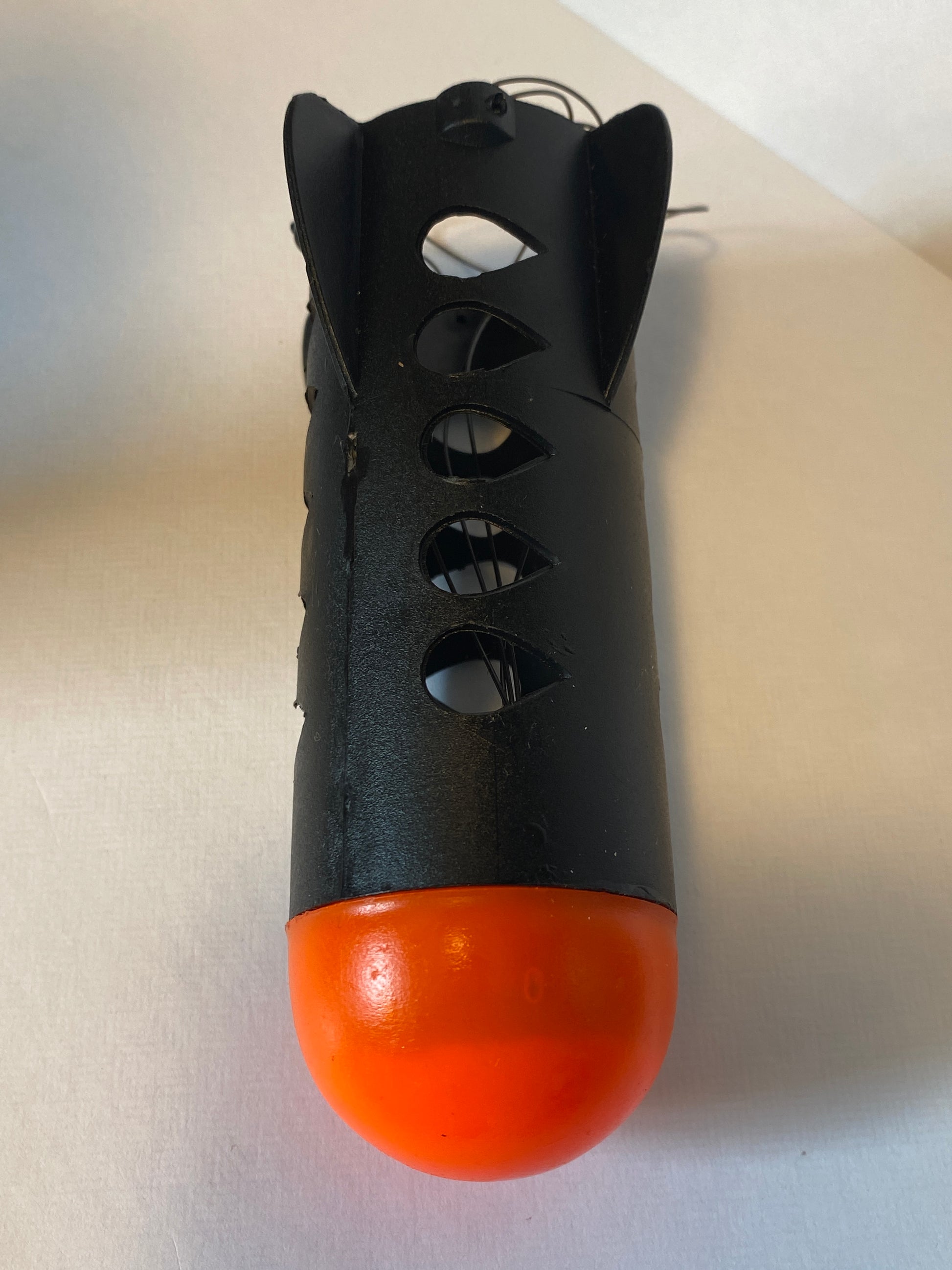 Black and orange spod rocket with cut-out design on a light gray background