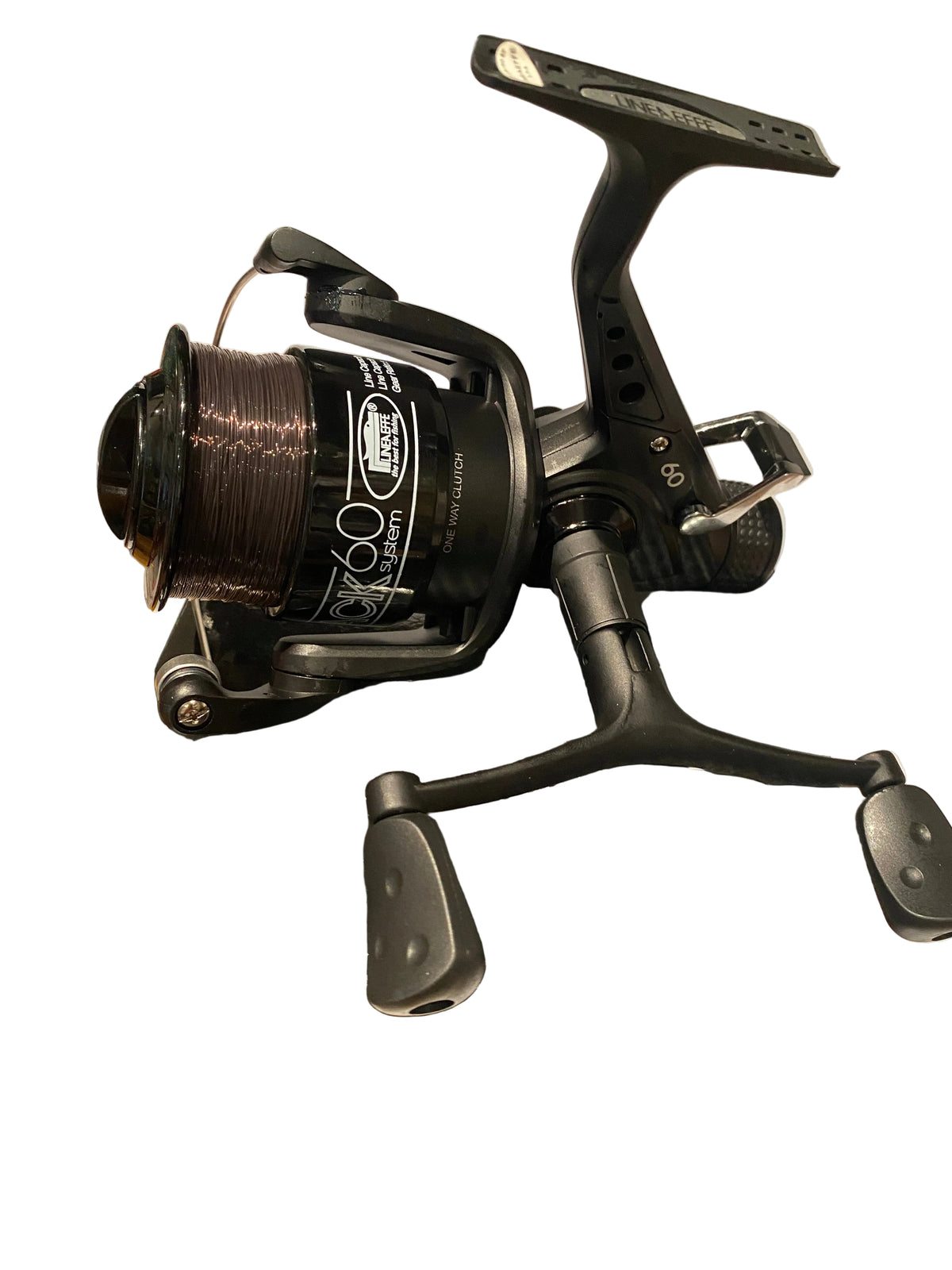 A black spinning fishing reel mounted on a black cardboard box, photographed on a white surface with some surrounding clutter visible.