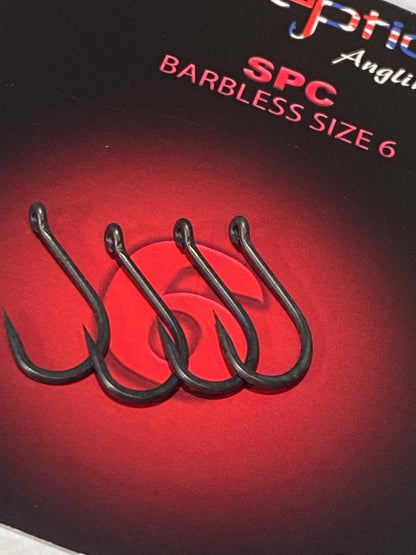 Four black barbless fishing hooks arranged on a red and black package label with visible text reading 'Spc Angles Barbless Size 6'.