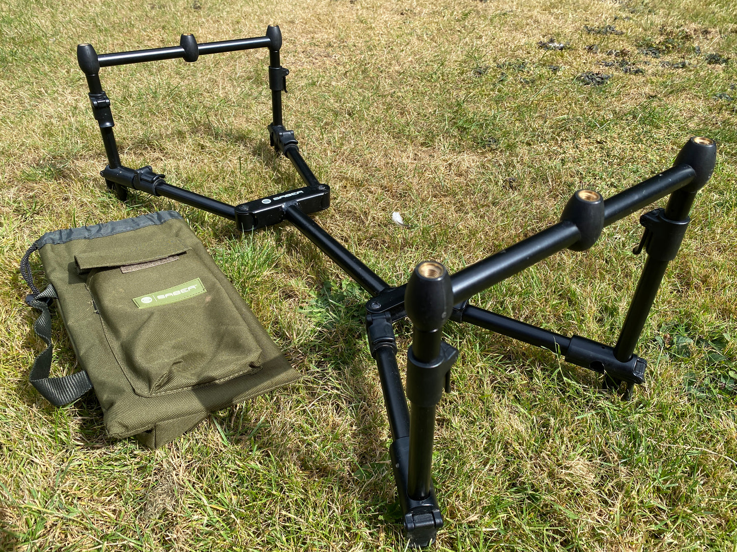 Black fishing rod pod on grass with green carry case
