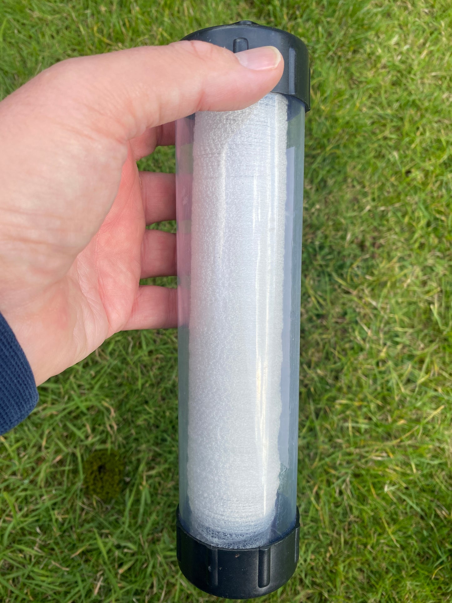 Hand holding a tube of PVA mesh against a grass background